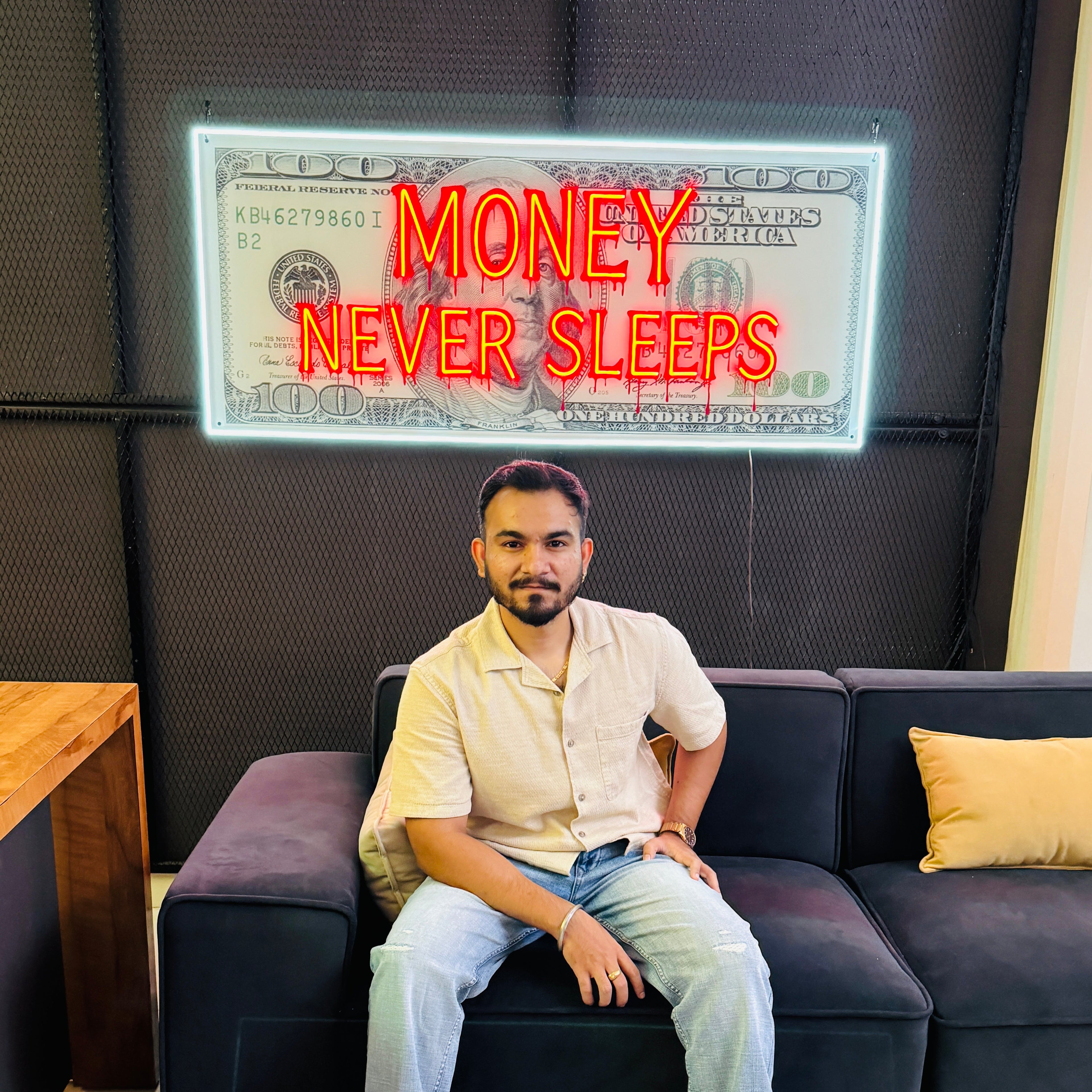 Man sitting on a couch with a large dollar bill graphic and 'Money Never Sleeps' text in the background.