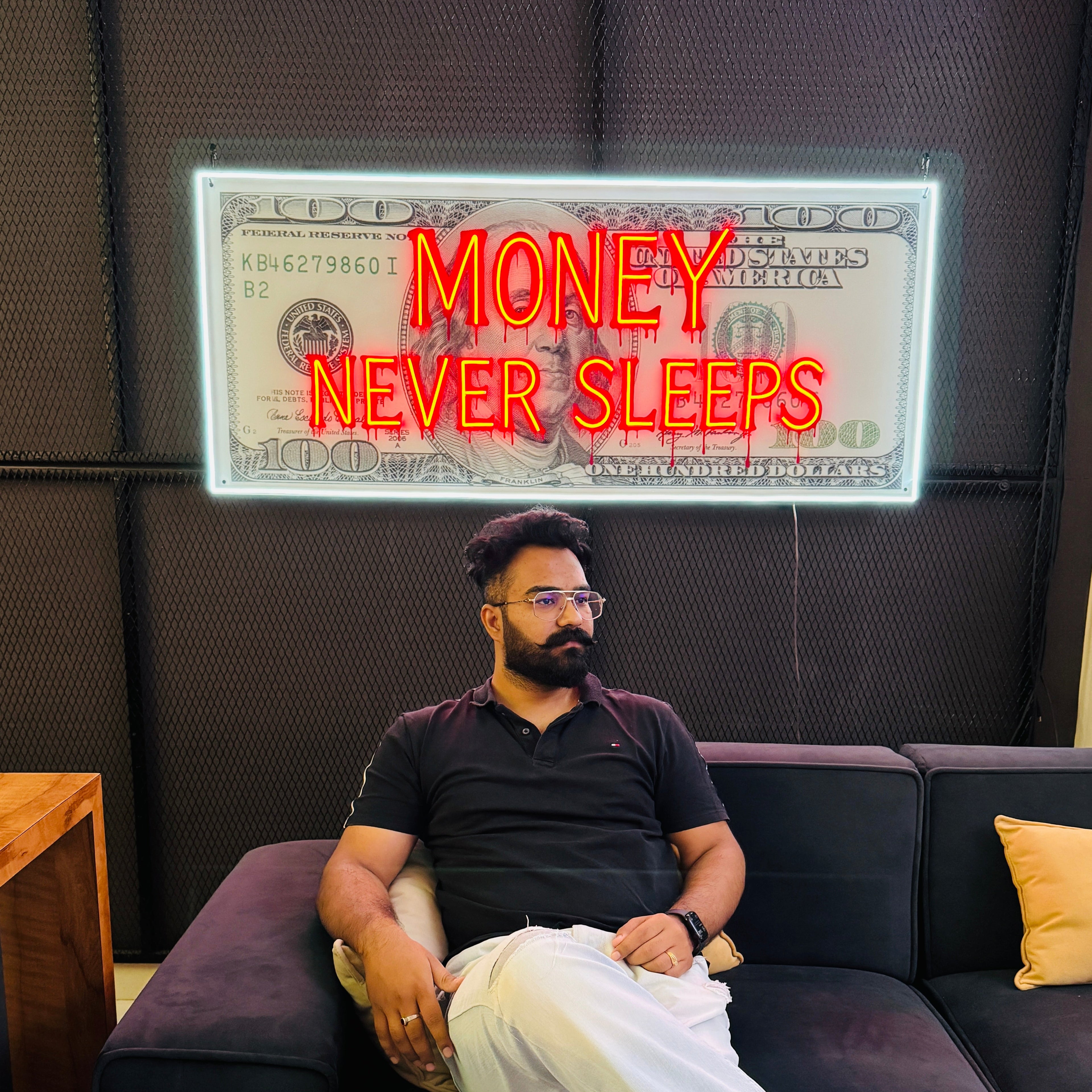 Man sitting on a couch with a dollar bill and 'Money Never Sleeps' text in the background